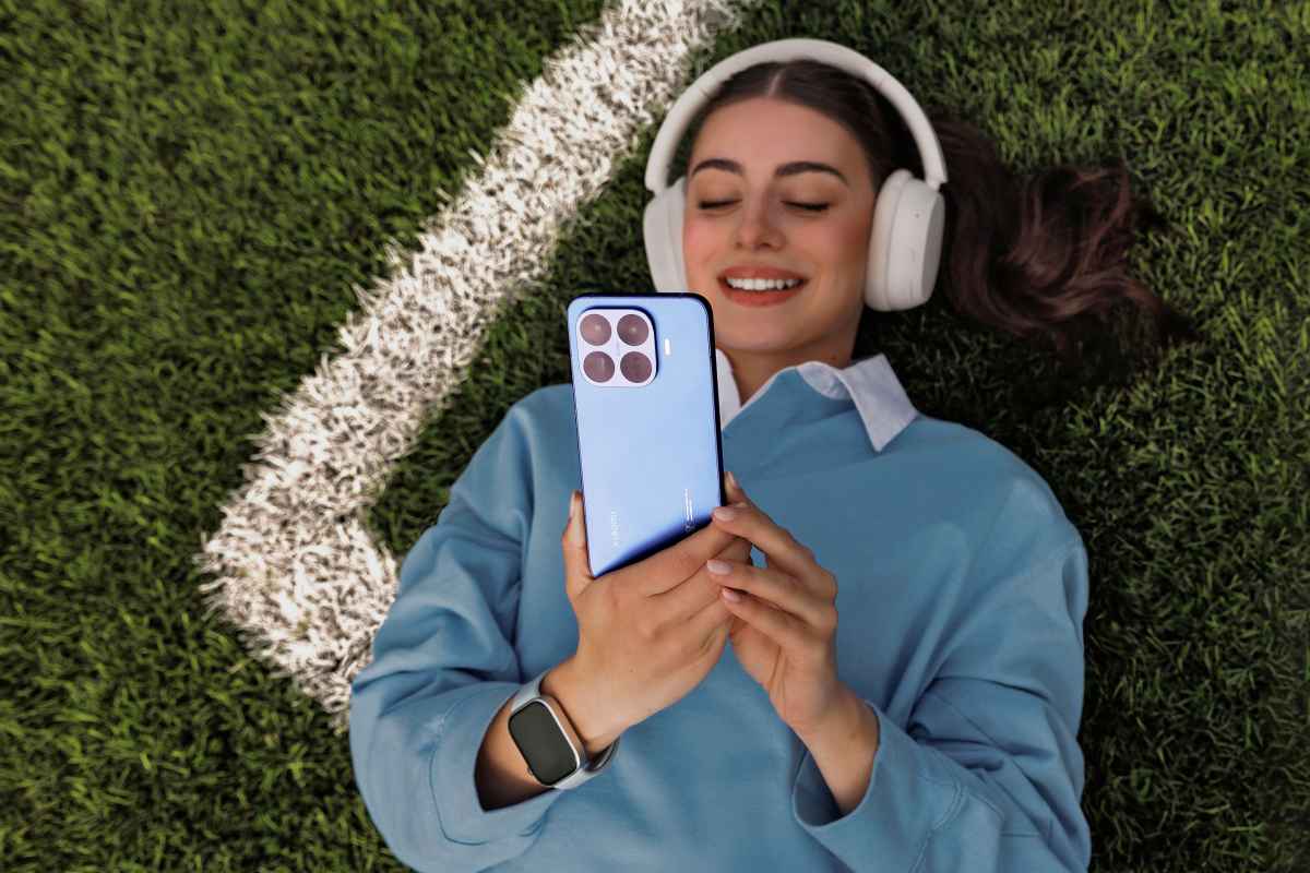 Moteris guli ant žolės su ausinėmis ir laiko telefoną.